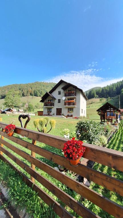 a wooden fence with flowers and a house in the background at Cabana Inima Munților in Gârda de Sus