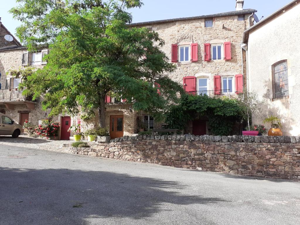 un edificio de piedra con ventanas rojas y pared de piedra. en Maison de caractère au cœur des grands causses, en Viala-du-Tarn