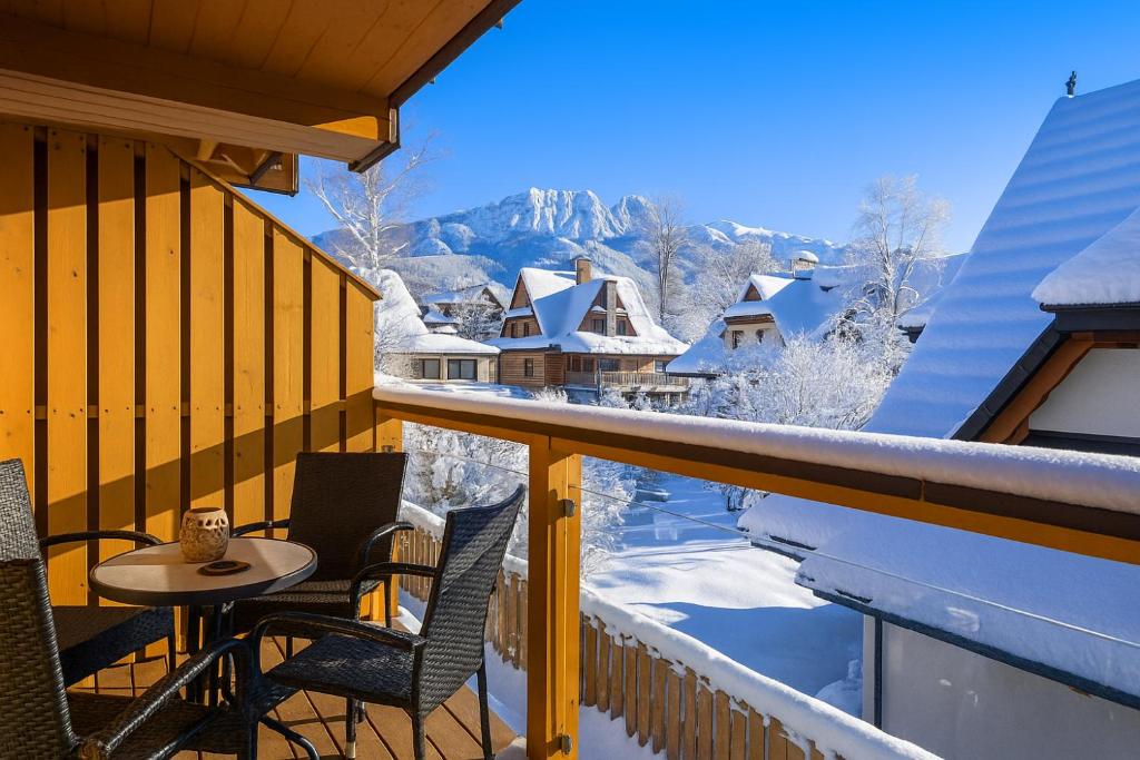 ザコパネにあるModrzejewska Residence Apartament z Góralką Giewont View by RentiloPLのテーブルと椅子のあるバルコニーと雪に覆われた建物