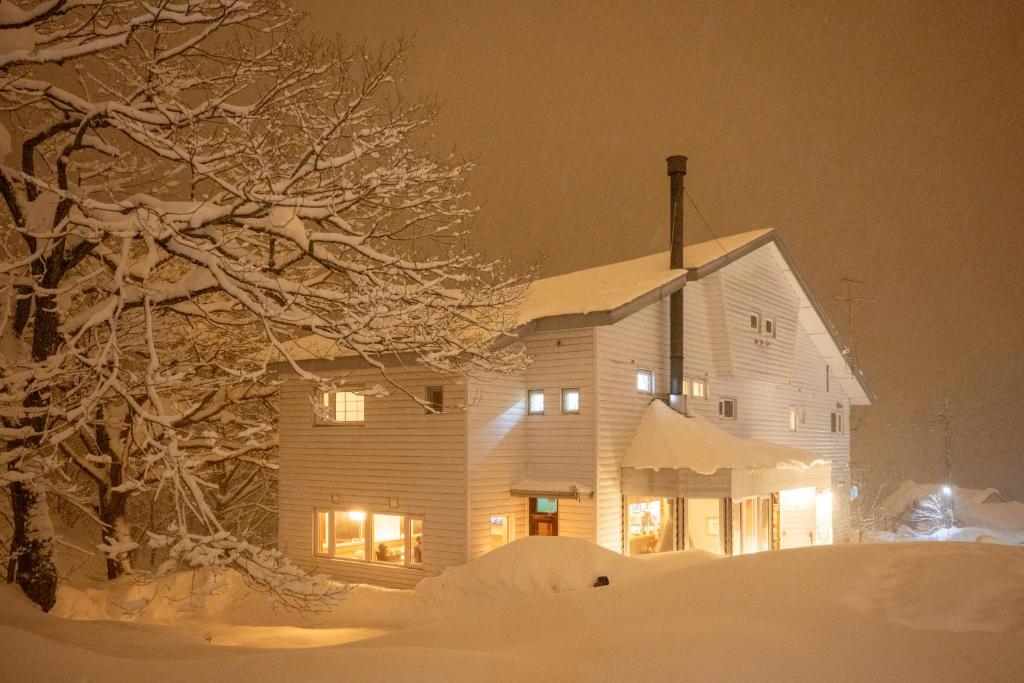 une maison recouverte de neige la nuit avec des lumières dans l'établissement Raicho Lodge Madarao, à Iiyama