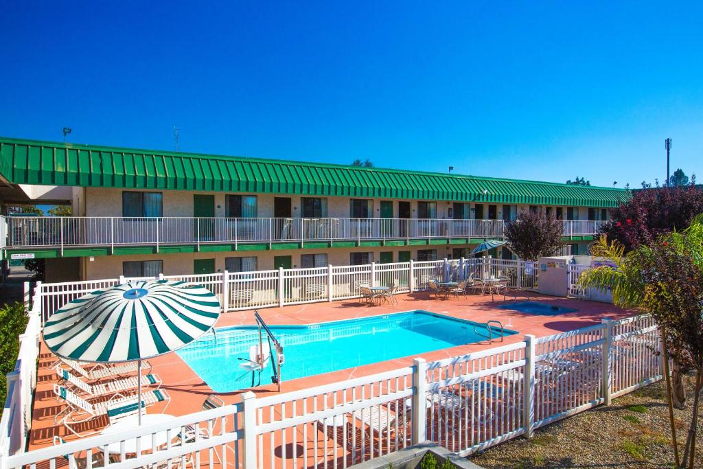 a hotel with a swimming pool and an umbrella at University Inn Fresno in Fresno