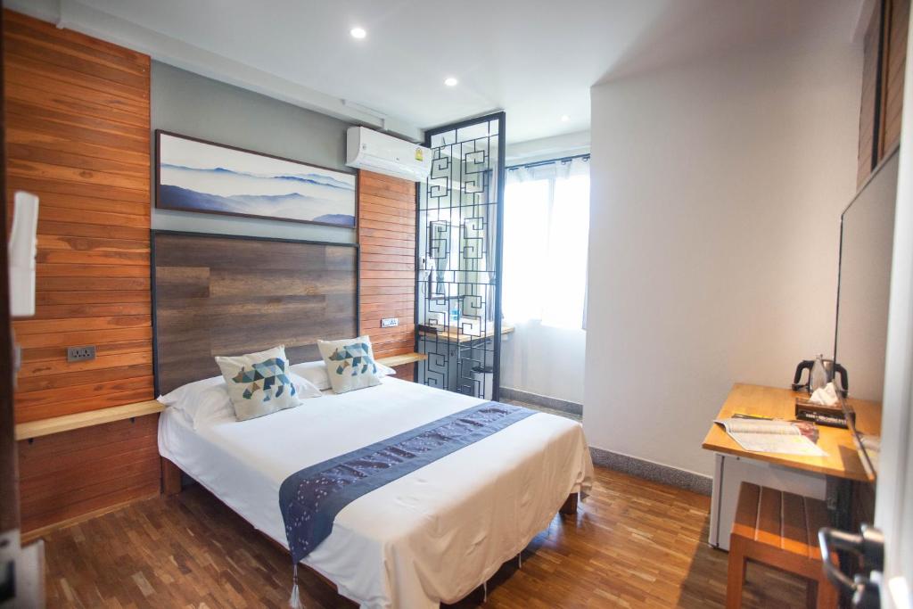 A compact double room with a desk, wood paneling, and a bright window.