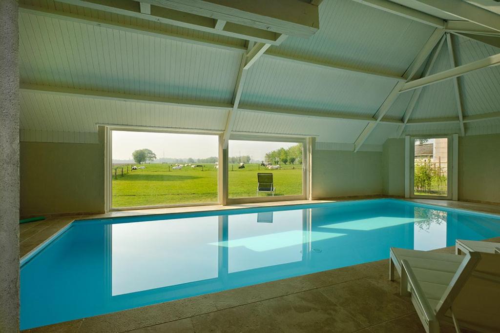 a large swimming pool in a house with a large window at Domein Het Weiland in Damme