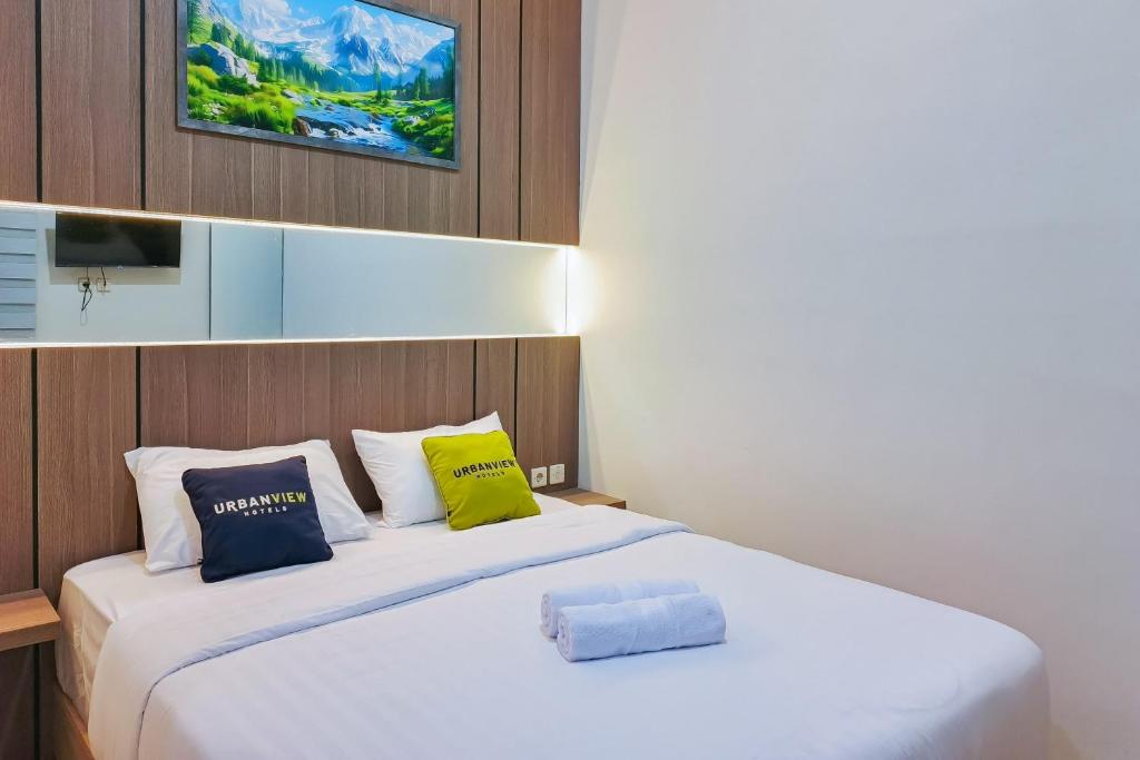 a bedroom with a white bed with yellow and blue pillows at Urbanview SANT Hotel Syariah near Stasiun Tegal in Tegal
