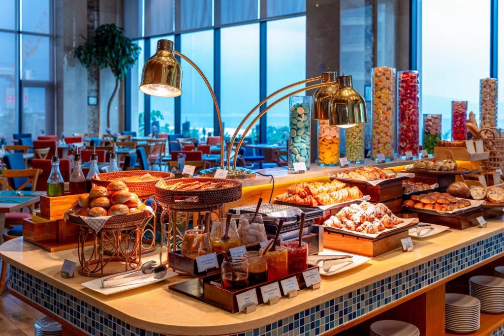 A broad breakfast buffet counter with pastries, breads, condiments and jars of cereal.