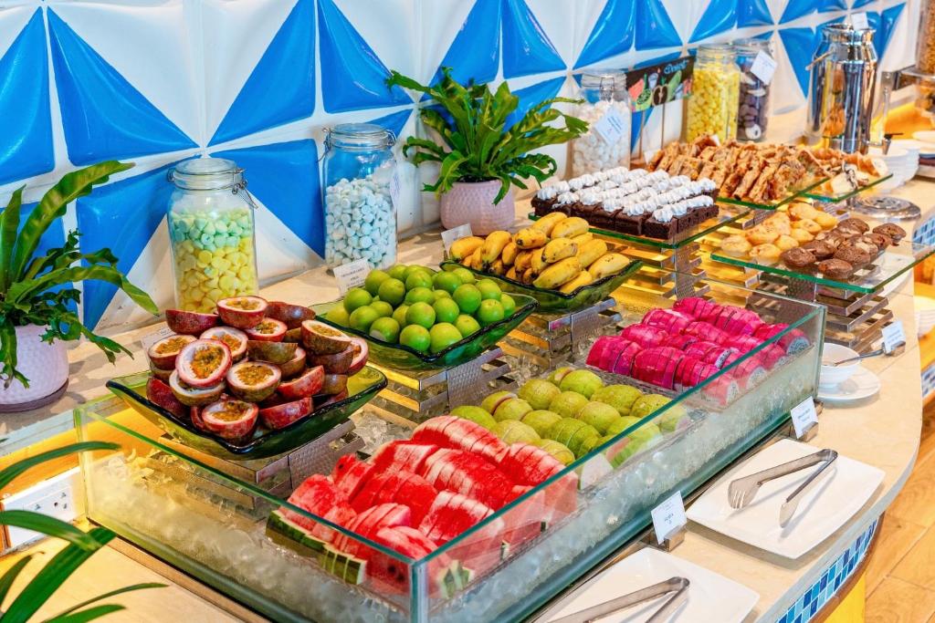 A chilled fruit display with tropical fruit, bananas and pastries behind it.