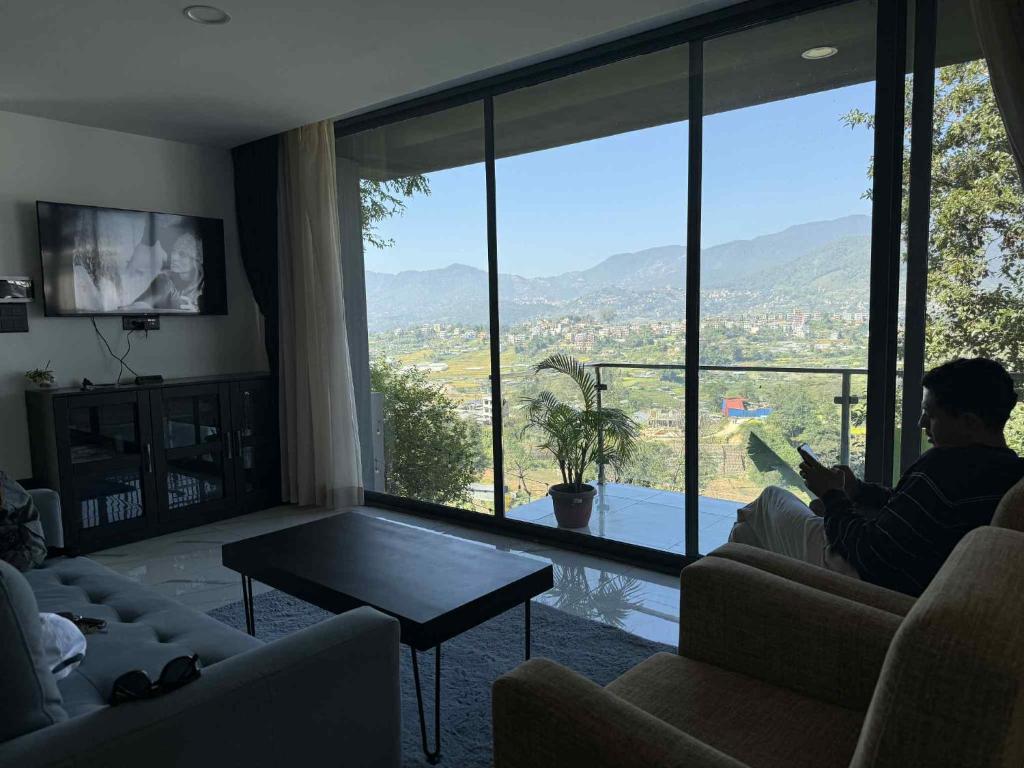 een man die op een bank zit in een woonkamer met een groot raam bij Villa by Bellavista in Pātan