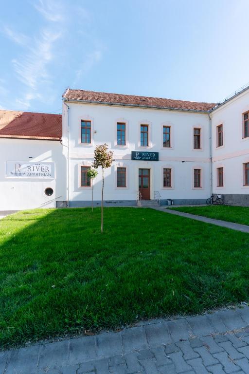 a building with a tree in the middle of a yard at River Apartmanház in Jászberény
