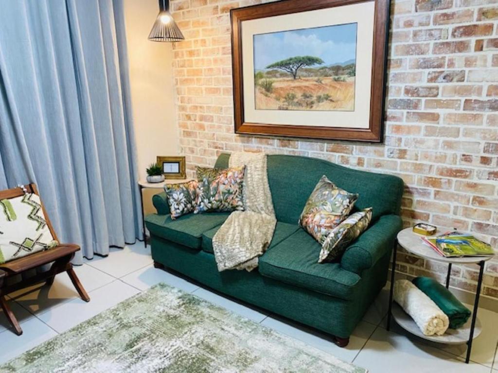 een groene bank in een woonkamer met een bakstenen muur bij Wild Olive at 51 in Windhoek