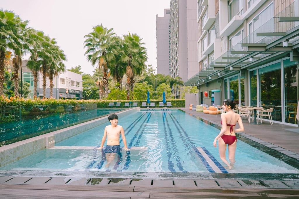 Guests use the hotel’s outdoor pool among palms and landscaped planting.