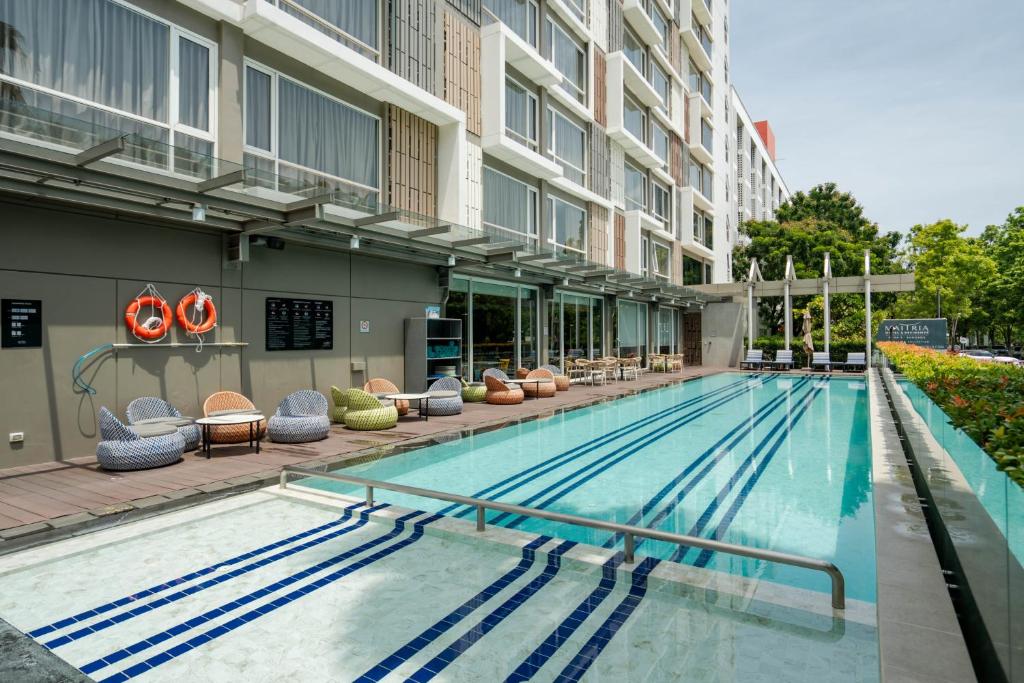 A long outdoor swimming pool beside the hotel building and a shaded seating deck.