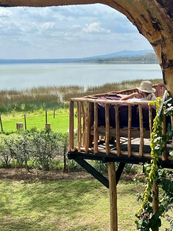 a man laying on a bed next to a body of water at TREE HOUSE Lodge in Gilgil