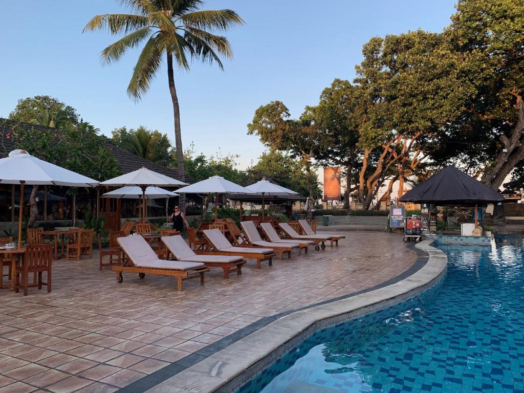 een rij stoelen en parasols naast een zwembad bij The Jayakarta Residence 2BR Bali in Denpasar