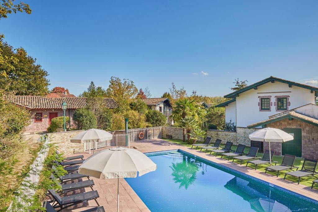 ユリューニュにあるVillas Odalys Le Domaine de Lanaの家の隣にある椅子とパラソルのあるプール