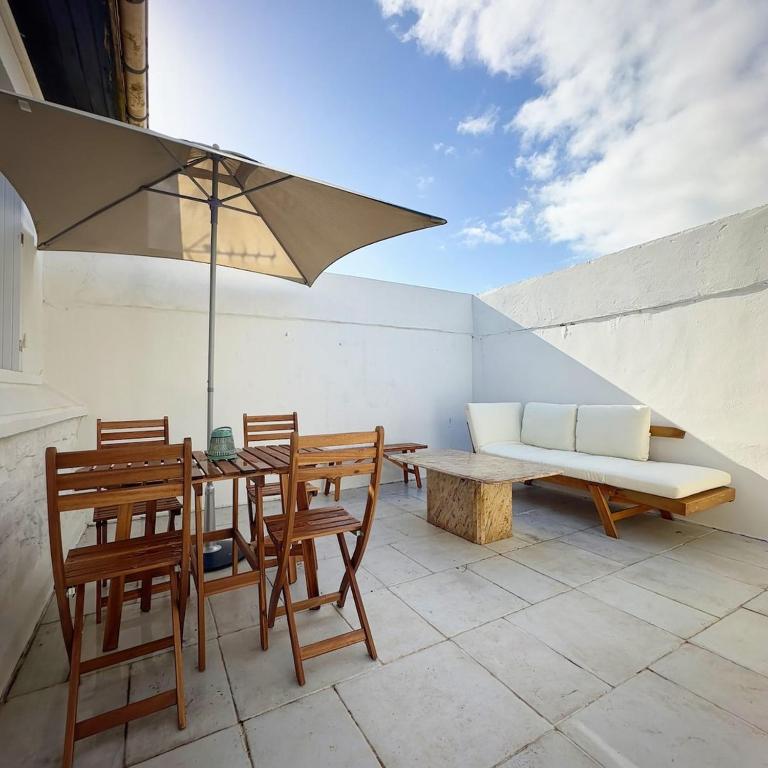 a patio with a table and chairs and an umbrella at Maloquet, maison chaleureuse proche Île de Ré in La Rochelle