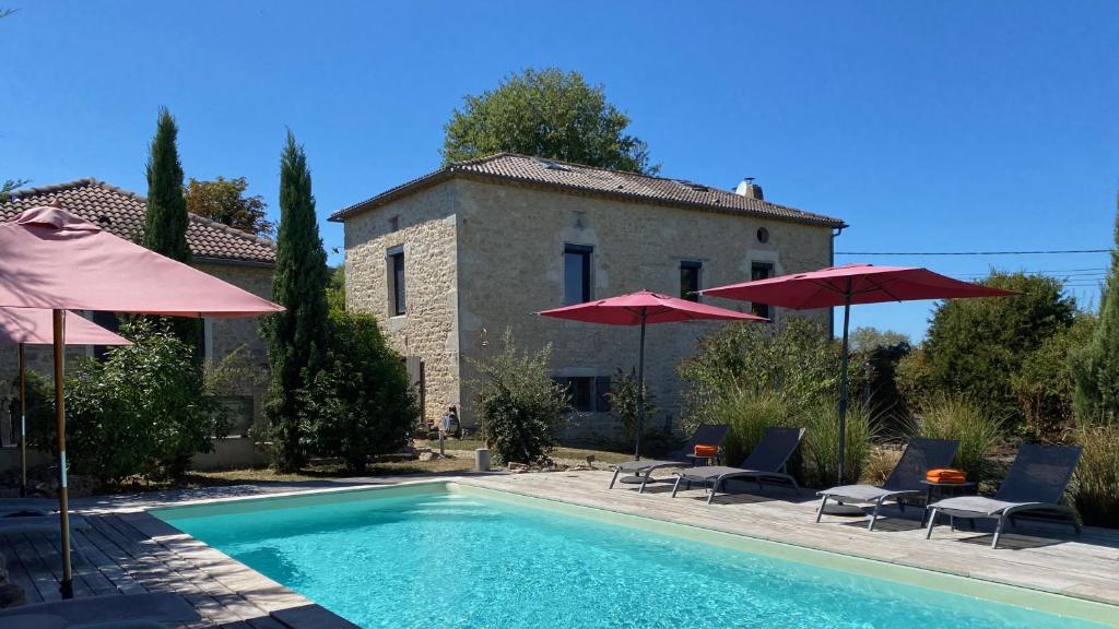 a swimming pool with umbrellas and chairs and a house at Maison Reces in Floressas