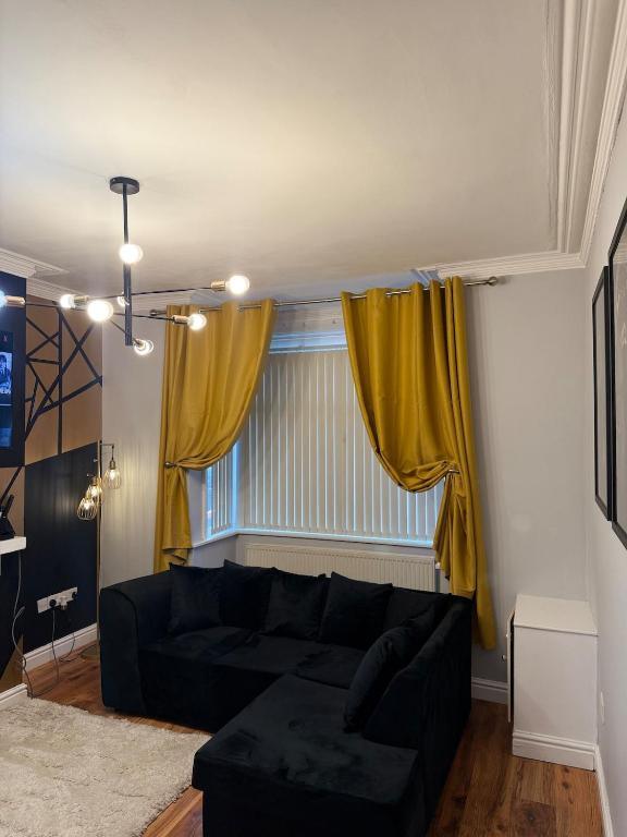 a living room with a black couch and yellow curtains at Stylish 3 BR home & Game room & Family Lounge in Dudley