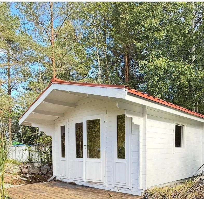 ein kleiner weißer Schuppen mit rotem Dach in der Unterkunft Glamping in a Bungalow Deluxe by the Forest w Swimmingpool near Golf and the Baltic Sea Beach in Järna