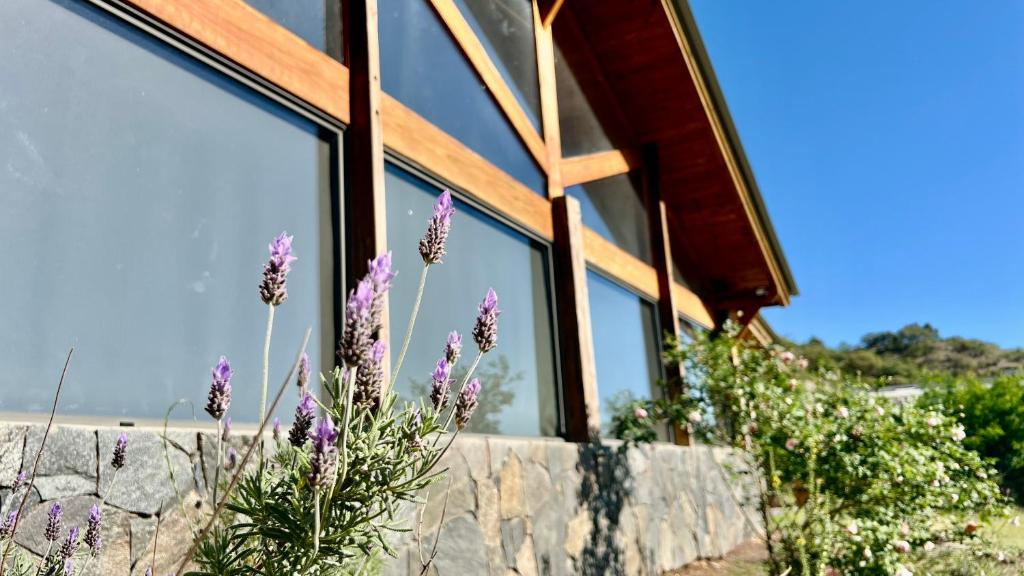 a house with a stone wall and purple flowers at Fincas del Faldeo in Villa General Belgrano