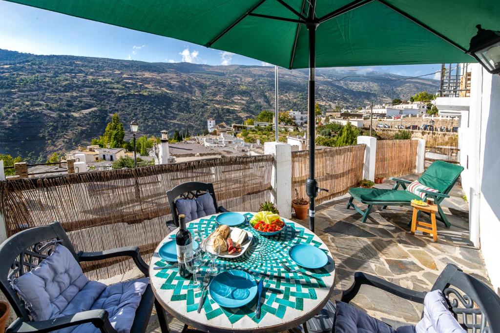 a table and chairs with a green umbrella on a patio at Casa La Soleá. Vistas al pueblo y la Sierra in Bubión