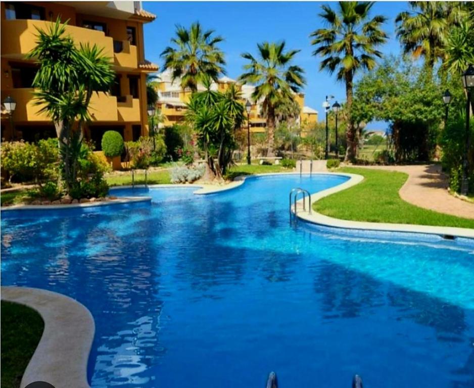 a swimming pool in front of a building with palm trees at Elegant Penthouse with Private Rooftop Punta Prima in Torrevieja
