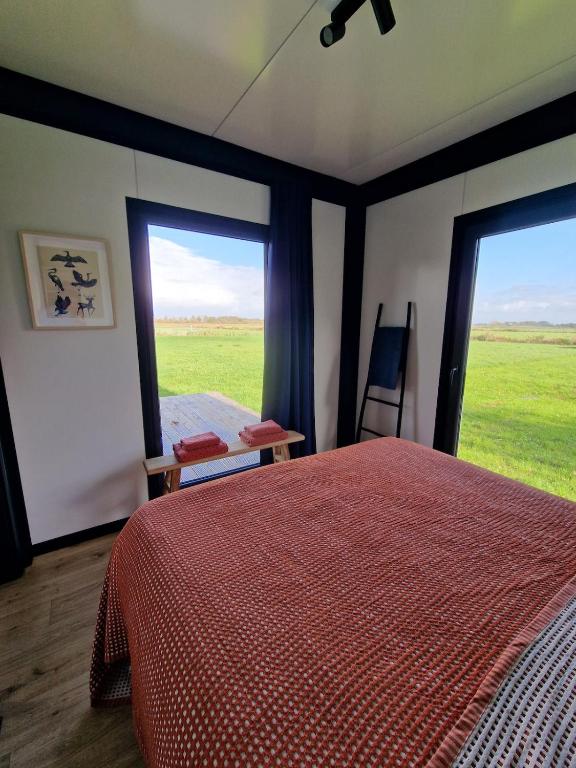 a bedroom with a bed and two large windows at Tiny house Polderzicht in De Veenhoop