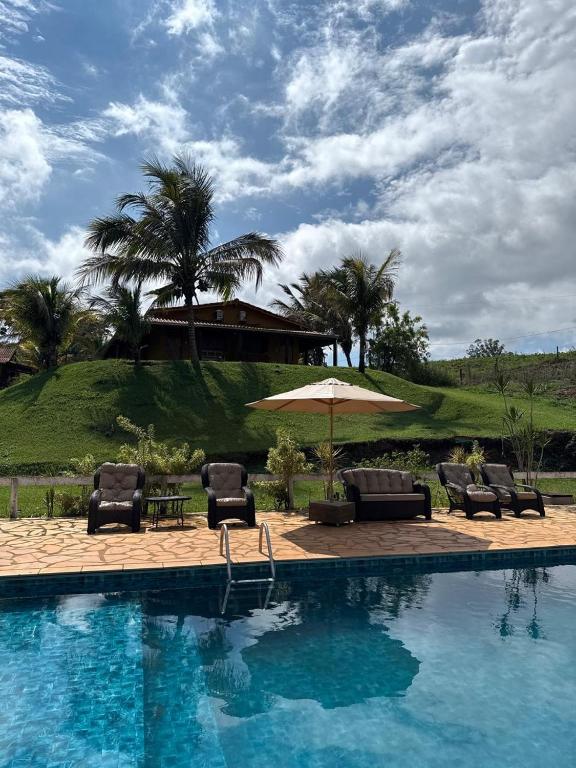 a swimming pool with chairs and an umbrella at Pousada Ana Maria in Delfinópolis