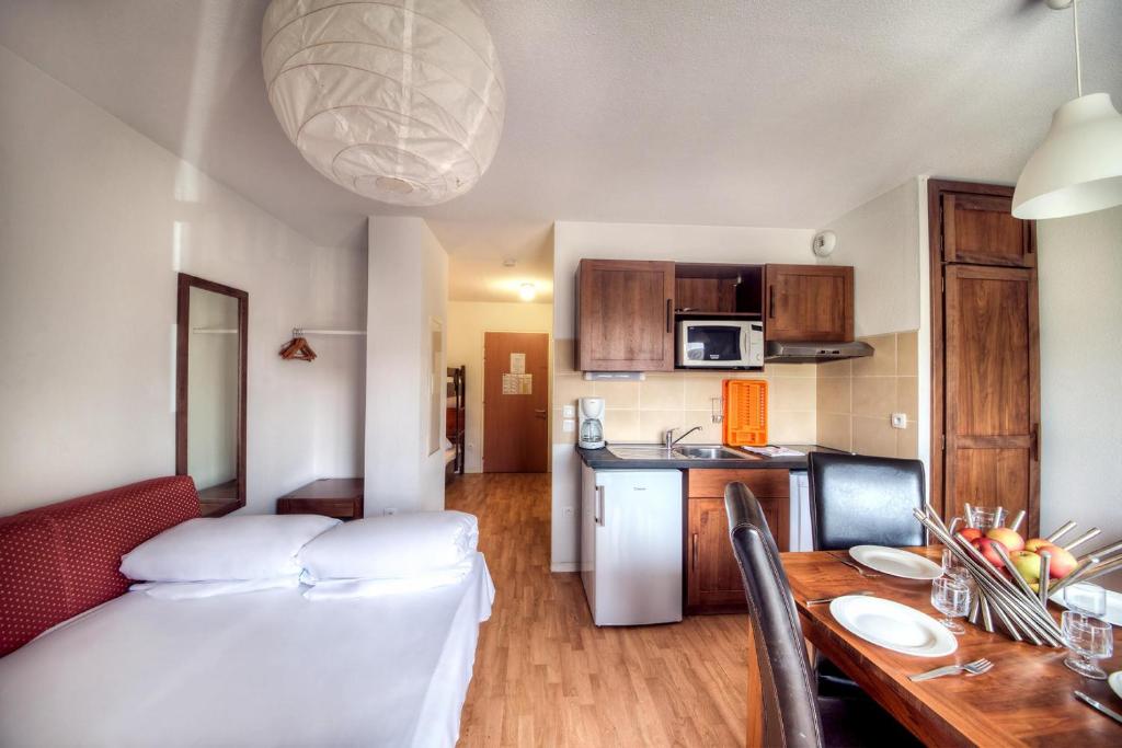 a kitchen with a large bed and a white refrigerator at Zenitude Hôtel-Résidences l'Acacia Lourdes in Lourdes