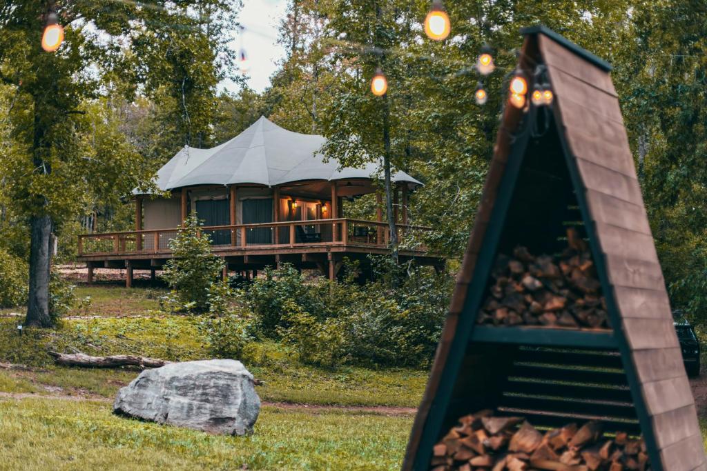 a house in the woods with a pile of fire wood at Luxuring Glamping Tent - The Dog Wood - Near Tryon International Equestrian Center - Wheat Creek Outpost in Mill Spring