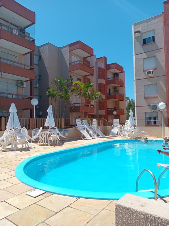 une grande piscine avec des chaises et un bâtiment dans l'établissement Apartamento Capão Novo, à Capão Novo