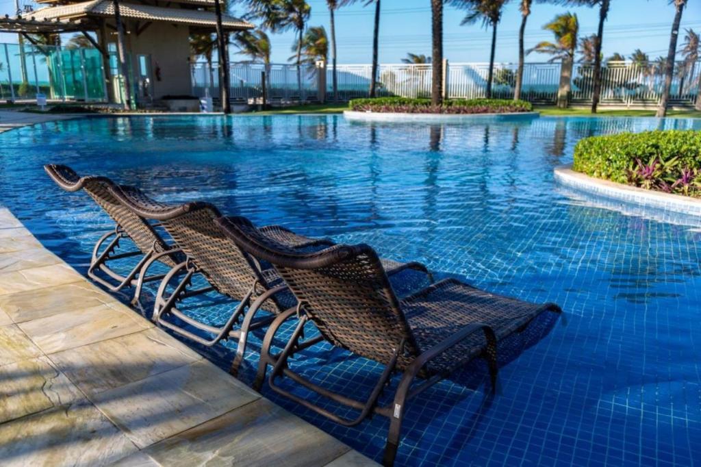 a swimming pool with two chairs in the water at Golf Ville Resorts 1 km Beach park in Aquiraz