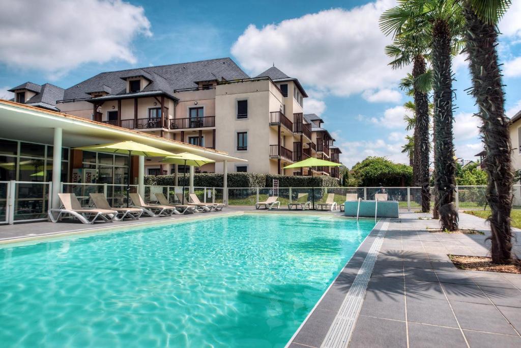 une piscine avec des palmiers en face d'un hôtel dans l'établissement Zenitude Hôtel-Résidences l'Acacia Lourdes, à Lourdes