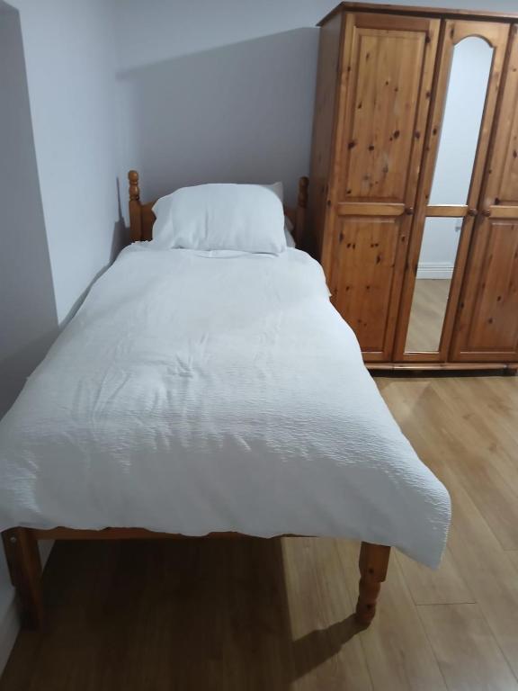 1 cama con colcha blanca y armario de madera en A1 apartment, en Loughrea