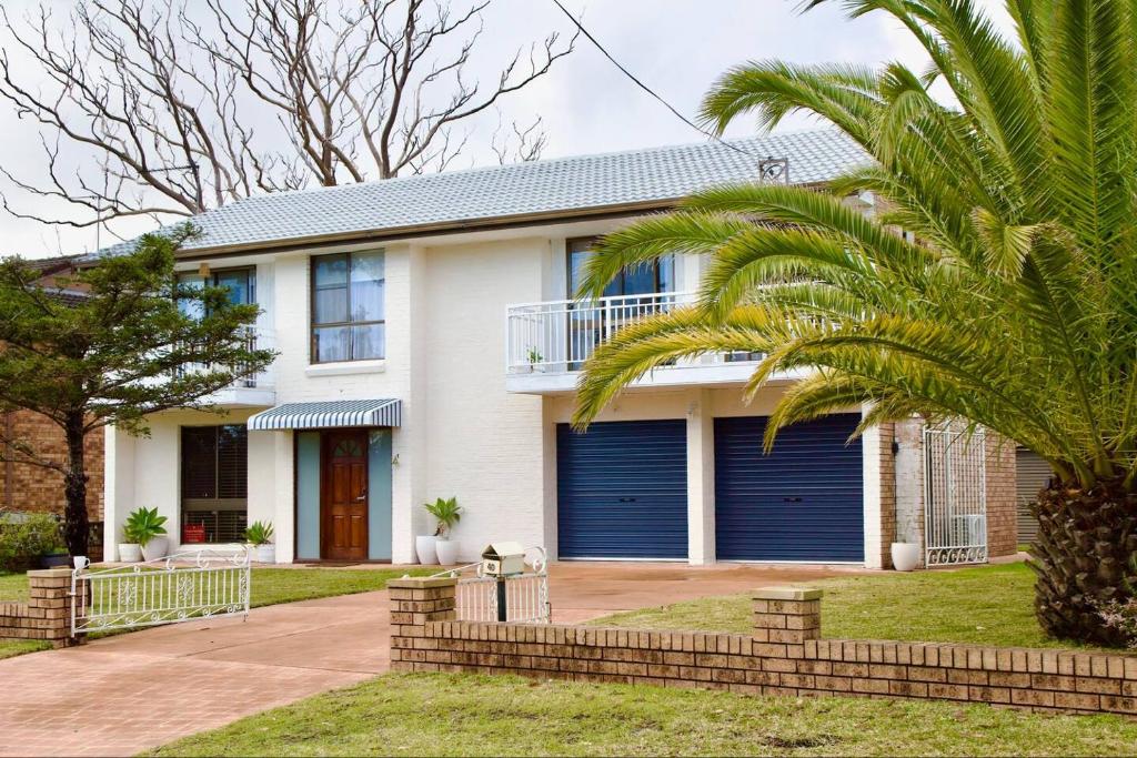 Una casa con puertas de garaje azules y una palmera. en Lilly Pilly at Callala Beach, en Callala Beach