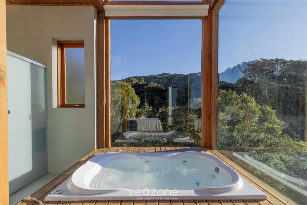 a bath tub in a room with a large window at Chalé na serra com Vista Magnífica VST017 in São Paulo dos Pinhais