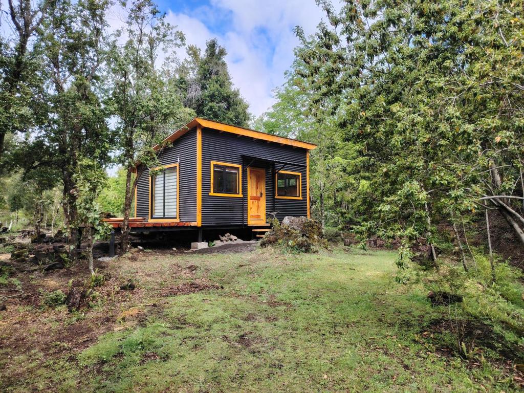 a small yellow and black house in the woods at Cabañas Del Monte 2 in Melipeuco