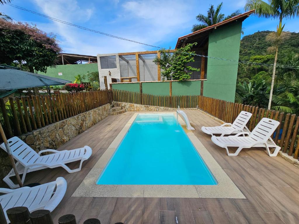 a swimming pool with two chairs and a table and a house at Chalé dos Açaís próximo à Trindade in Paraty