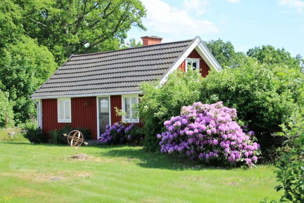 a small red house with purple flowers in the yard at Sommargyllen Torp Brändabo Småland Kalmar Öland in Torsås