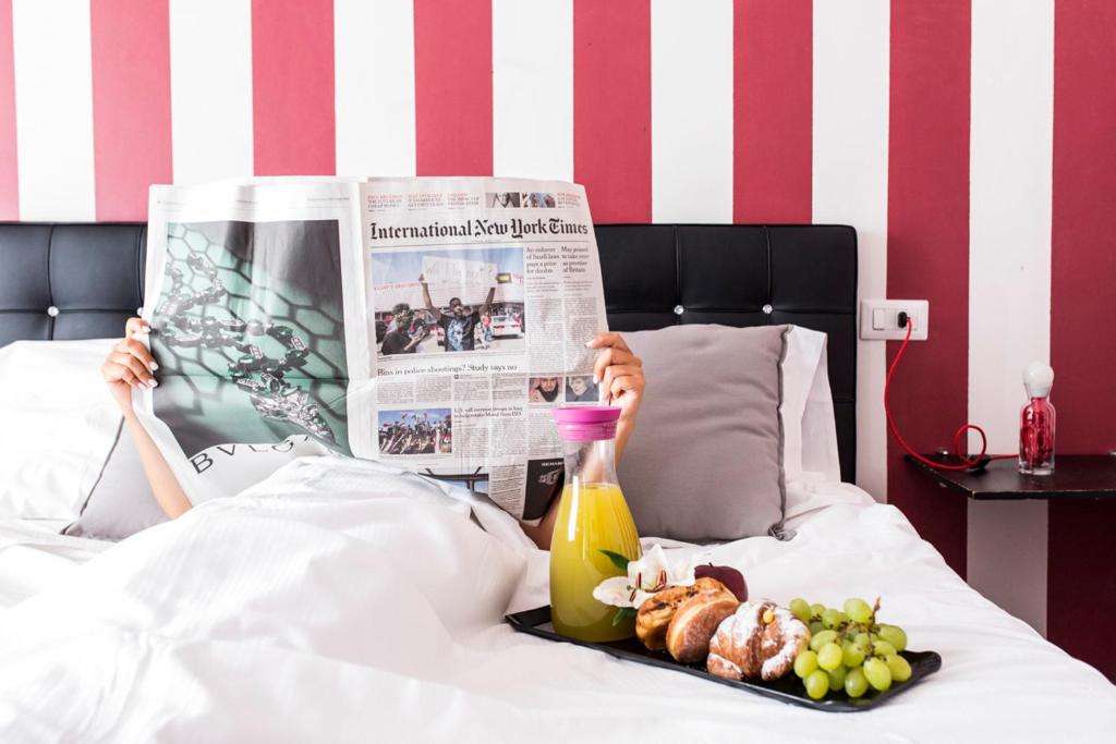 una persona sdraiata a letto che legge un giornale con un vassoio di cibo di Il Giglio Rosso B&B a Firenze
