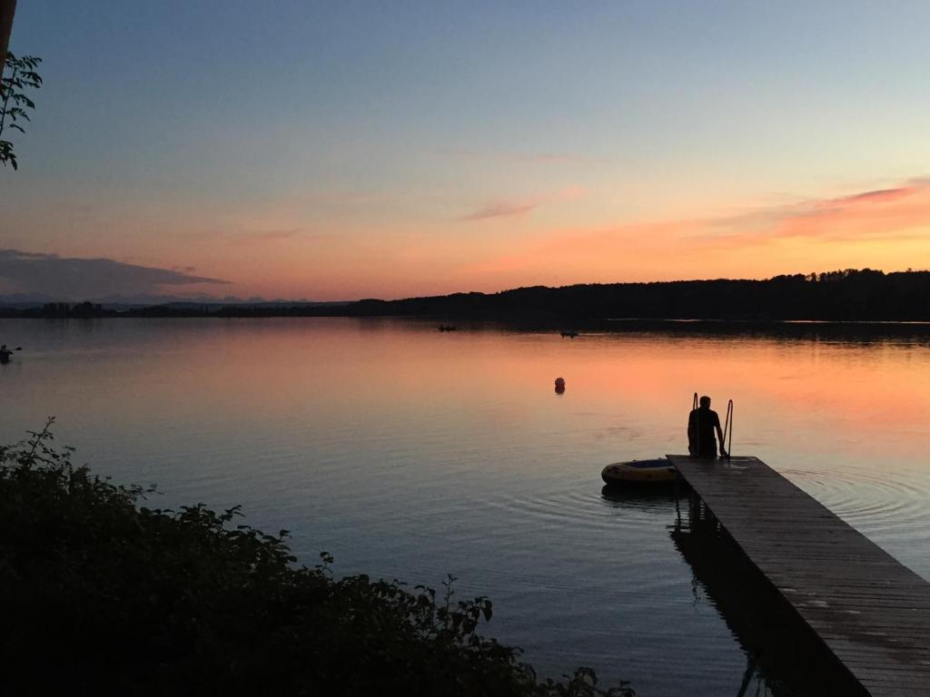 Ein Mann, der bei Sonnenuntergang auf einem Dock auf einem See sitzt. in der Unterkunft Chalet am Pilsensee in Seefeld