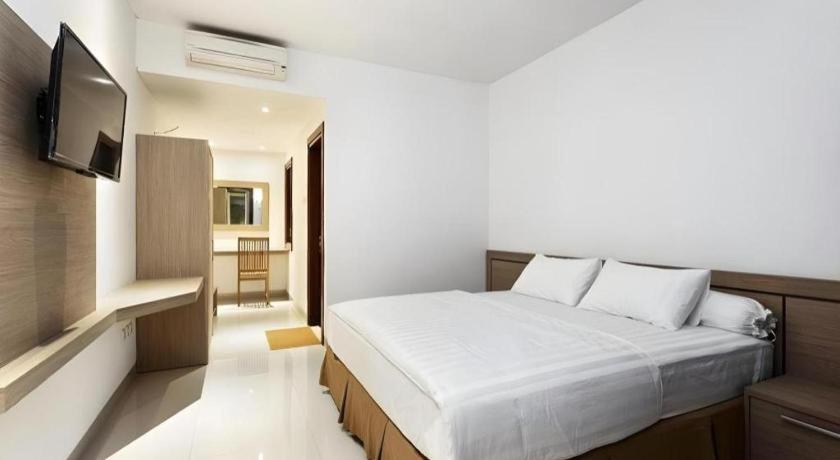 a bedroom with a white bed and a television at Hotel Adilla Syariah Ambarukmo in Yogyakarta