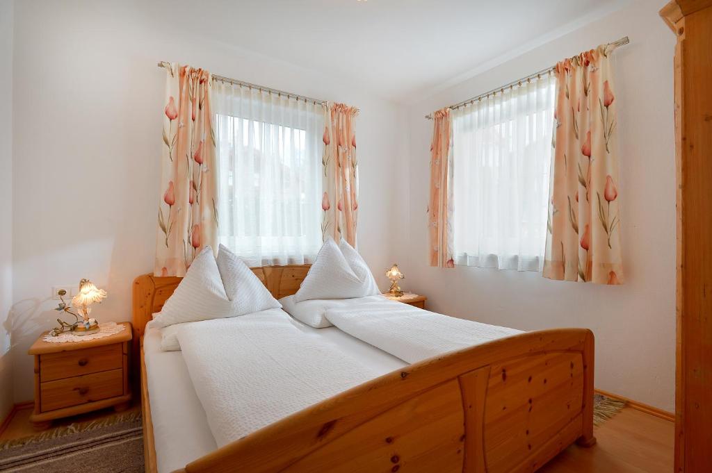 a bedroom with a wooden bed with two windows at Appartement Horngacher in Scheffau am Wilden Kaiser