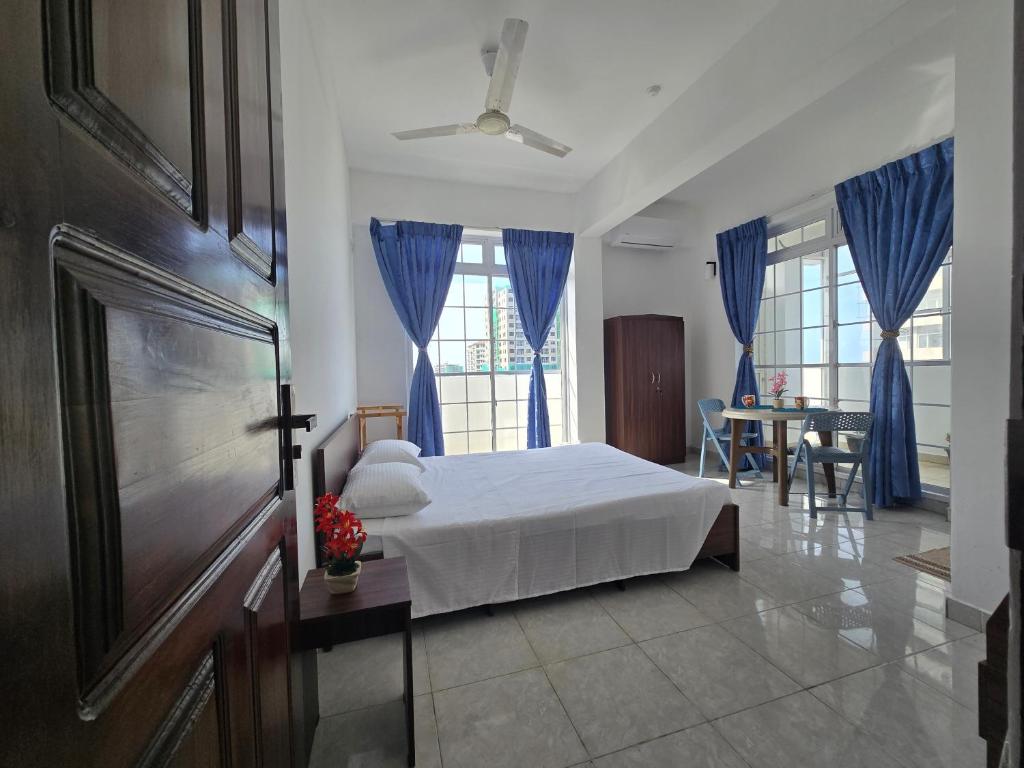 a bedroom with a bed with blue curtains and a table at Beachfront City Escape Sunset Balcony AC WiFi in Colombo