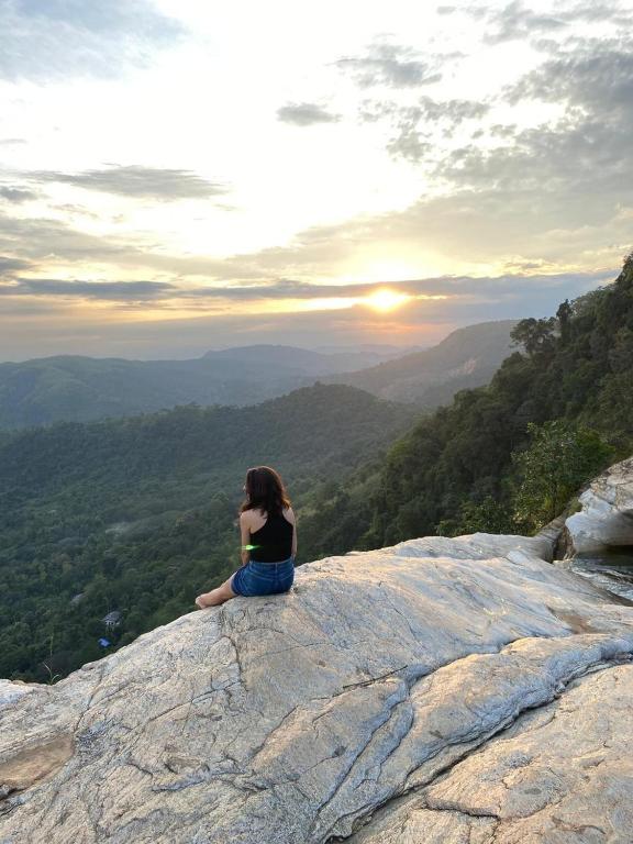 Eine Frau sitzt am Rand eines Felsens und beobachtet den Sonnenuntergang. in der Unterkunft Diyaluma Villa Resort in Koslanda