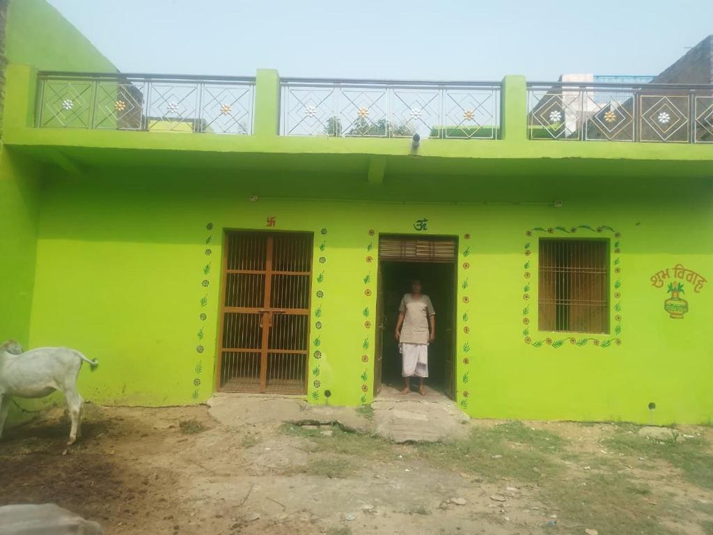a woman standing in the doorway of a green house at Ramanuj Rural Homesty in Raipura