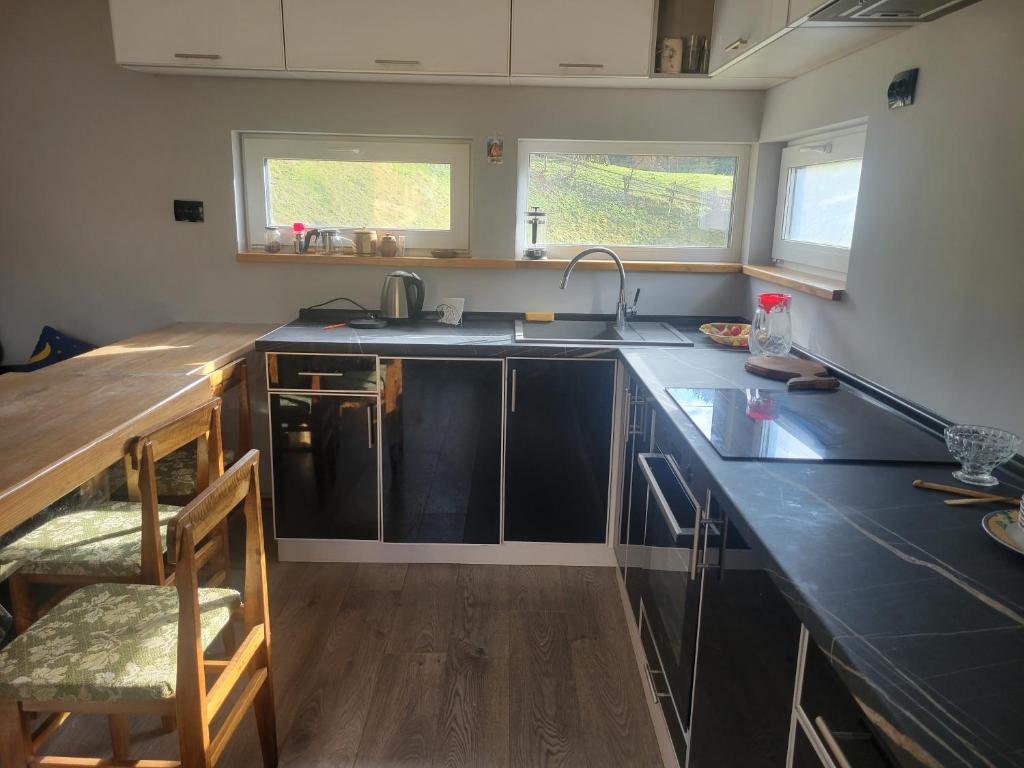 Una cocina con encimeras negras, un fregadero y dos ventanas. en Забрус насолоди, en Kosiv