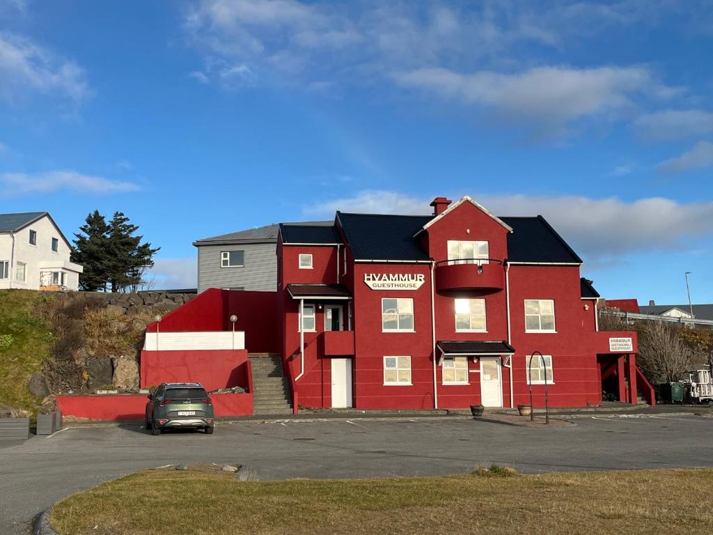 a red building with a car parked in a parking lot at Guesthouse Hvammur by the Harbour in Höfn