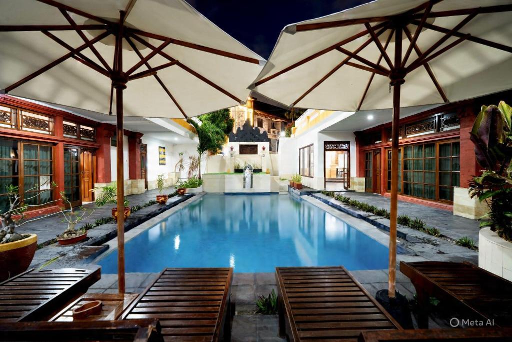 a swimming pool with two umbrellas and benches at Natasya Kuta Beach Hotel in Kuta