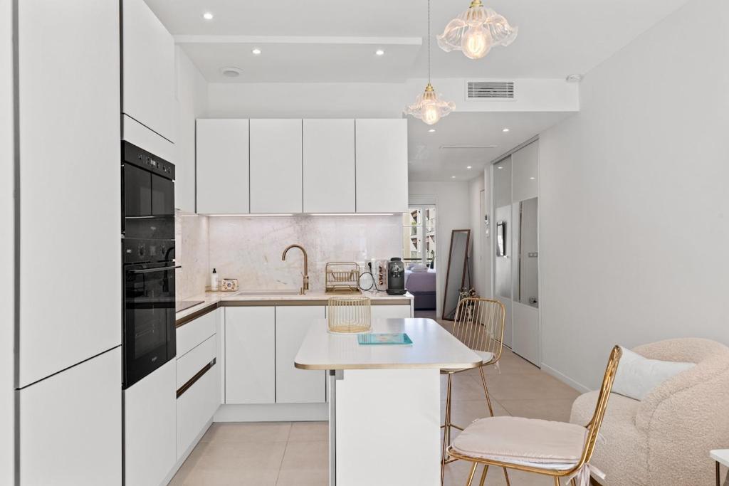 Una cocina con gabinetes blancos y una mesa y sillas. en 3 pièces Juan les Pins Cosy et Luxueux, en Juan-les-Pins