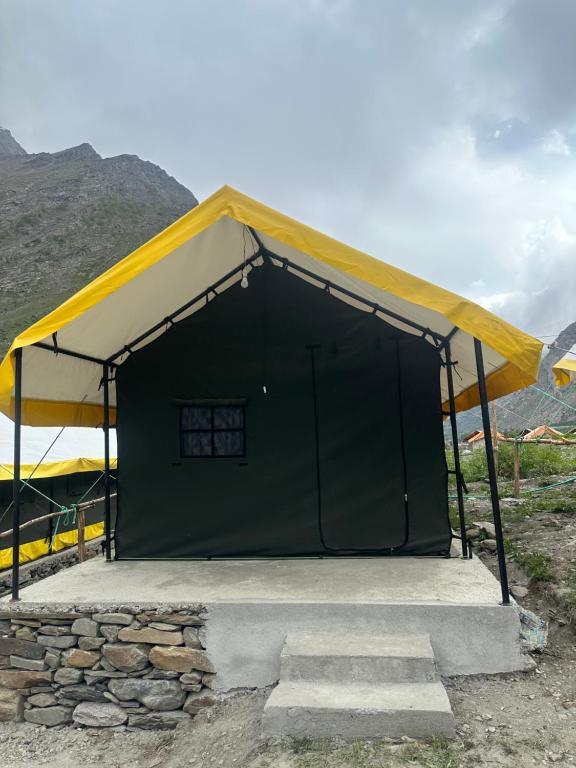 a green and yellow tent with a stone wall at River Rock Camps in Jispa